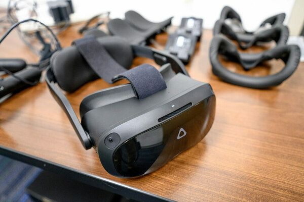 A wood-grain table with multiple sets of black VR goggles placed in rows.