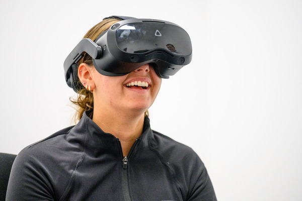 A smiling young woman looks up while wears a set of black vr goggles.